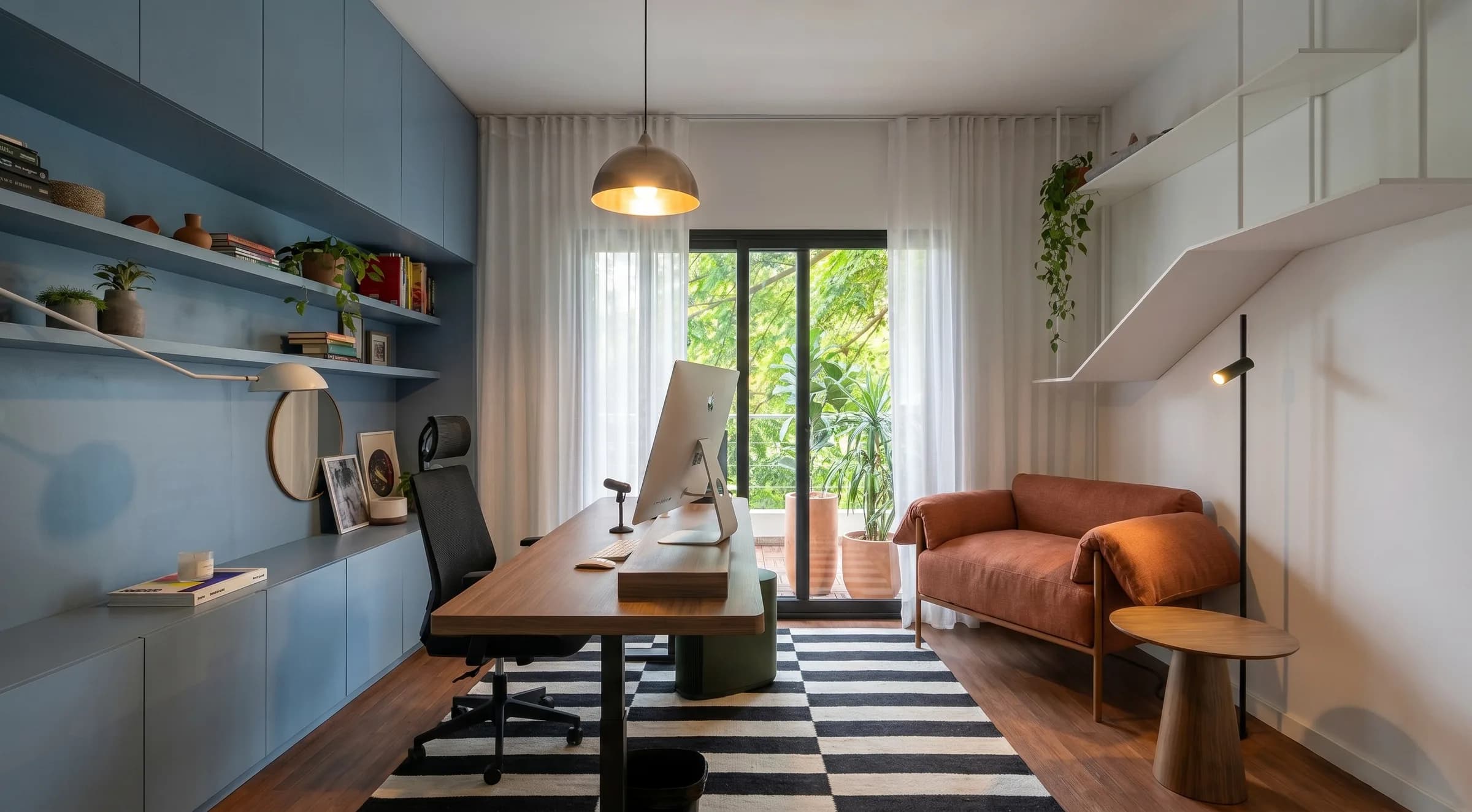 home office com parede azul, prateleiras, mesa de madeira e sofá terracota